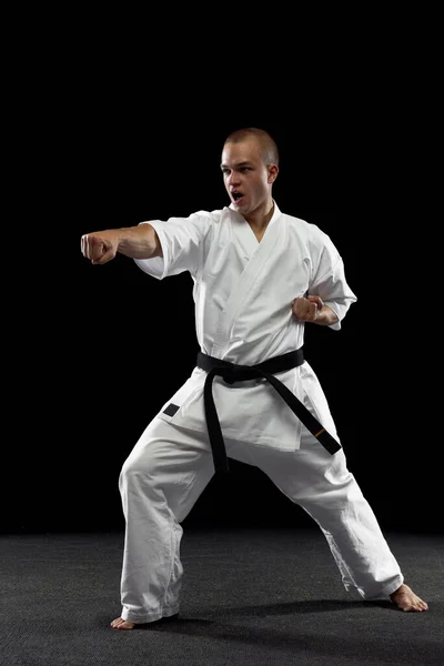 Fullängds porträtt av ung idrottsman utbildning karate isolerad över svart bakgrund. Rak punch pose — Stockfoto