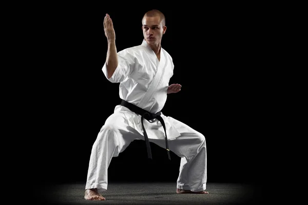 Full-length portrait of young sportsman training karate isolated over black background. Straddle stance pose — Stock Photo, Image