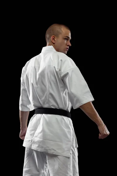 Vista trasera. Retrato recortado de deportista masculino en kimono blanco con cinturón negro aislado sobre fondo oscuro — Foto de Stock