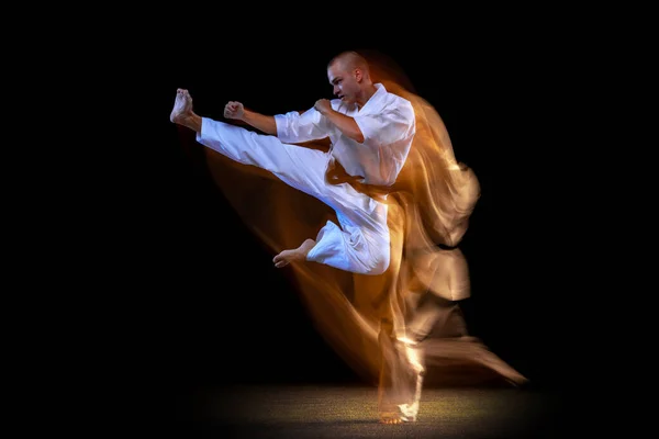 Ung kaukasisk idrottsman klädd i kimono praktiken i karate isolerad över svart bakgrund. Blandad ljuseffekt — Stockfoto