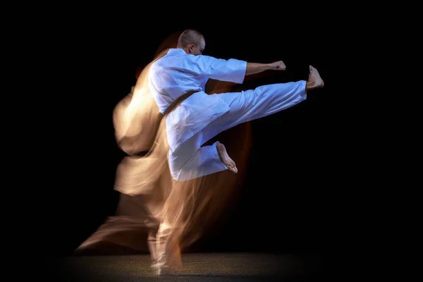 Baksidan visa porträtt av karate idrottsman utövar isolerade över svart bakgrund. Blandad ljuseffekt — Stockfoto