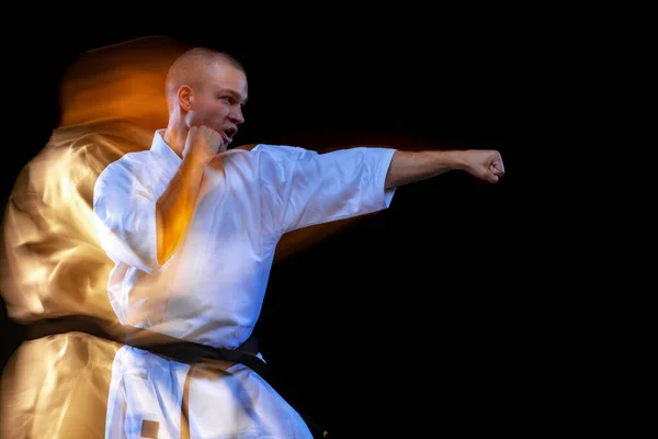 Gesneden portret van jonge karate sportman met witte kimono geïsoleerd over zwarte achtergrond. Gemengd lichteffect — Stockfoto