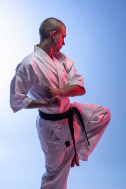 Yan görüş. Kavgada duran beyaz tenli bir sporcu gradiyet beyaz mavi arka planda izole bir poz veriyor. Karate, judo, tekvando sporu