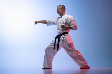 Bir kavgada duran yan görüş sporcusu gradiyet beyaz mavi arka planda izole bir poz veriyor. Karate, judo, tekvando sporu