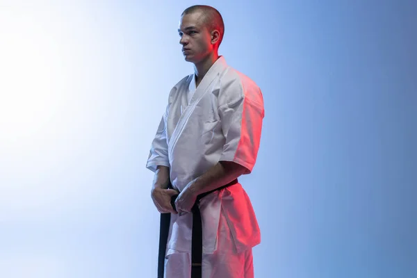 Widok z boku portret młodego profesjonalnego karate, judo sportowca w białym kimono izolowane na gradientowym białym tle niebieskim — Zdjęcie stockowe