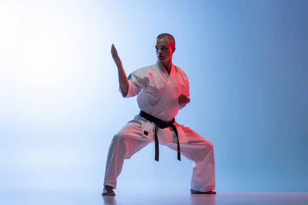 Full längd porträtt av kaukasisk idrottsman står i en kamp utgör isolerad över gradiet vit blå bakgrund. Karate, judo, taekwondo sport — Stockfoto