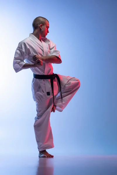 Teljes hosszúságú portré fiatal kaukázusi sportolóról, aki a karate, judo, taekwondo harcművészetét gyakorolja elszigetelve fehér kék alapon — Stock Fotó