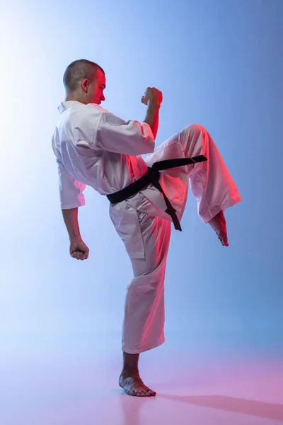 Teljes hosszúságú portré fiatal kaukázusi sportolóról, aki a karate, judo, taekwondo harcművészetét gyakorolja elszigetelve fehér kék alapon — Stock Fotó