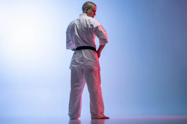 Baksidan visa fullängds porträtt av ung idrottsman i vit kimoto isolerade över lutning vit blå bakgrund. Karate, judo, taekwondo sport — Stockfoto