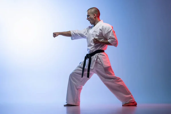 Bir kavgada duran yan görüş sporcusu gradiyet beyaz mavi arka planda izole bir poz veriyor. Karate, judo, tekvando sporu — Stok fotoğraf