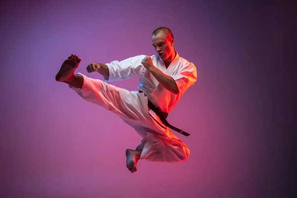 De jonge martial artist oefent vliegende trappen op een hellende roze achtergrond. Karate, judo, taekwondo sport — Stockfoto