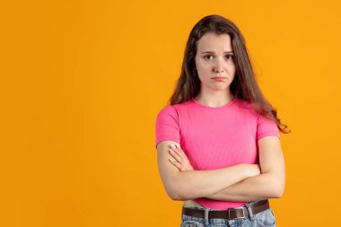 Pembe gömlek giyen güzel bir kızın portresi turuncu stüdyo arka planında izole edilmiş. Gücenmiş ifade