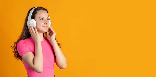 Vue de côté portrait recadré de jeune belle fille dans des écouteurs isolés sur fond de studio orange — Photo