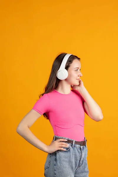 Boční pohled portrét mladé krásné dívky ve sluchátkách izolovaných přes oranžové studio pozadí — Stock fotografie