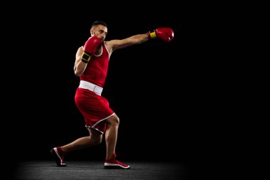 Siyah zemin üzerinde izole edilmiş kırmızı üniformalı profesyonel bir boksörün tam boy yan görünüm portresi. Düz yumruk hareketi. Sağlık, spor, hareket konsepti. İlan için alanı kopyala.