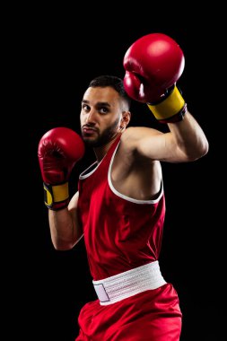 Yumruk atmaya hazırım. Siyah arka planda izole edilmiş kırmızı üniformalı bir boksörün portresi. Dövüşçü iş başında çalışıyor. Sağlık, spor, hareket konsepti. İlan için alanı kopyala.