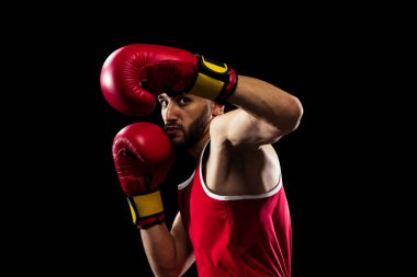 Kırmızı üniformalı ve boks eldivenli profesyonel boksör siyah arka planda izole edilmiş bir saldırıdan kaçınmak için el ele tutuşuyor. Dövüşçü iş başında çalışıyor. Sağlık, spor, hareket konsepti. İlan için alanı kopyala