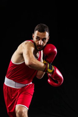 Kırmızı üniformalı ve boks eldivenli profesyonel boksör siyah arka planda izole edilmiş bir saldırıdan kaçınmak için el ele tutuşuyor. Dövüşçü iş başında çalışıyor. Sağlık, spor, hareket konsepti. İlan için alanı kopyala