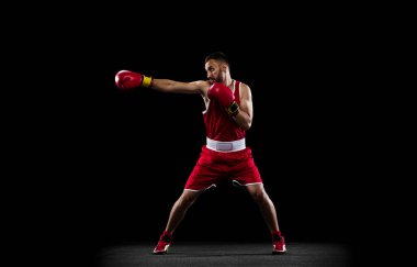 Siyah arka planda izole edilmiş kırmızı üniformalı profesyonel bir boksörün tam boy portresi. Düz yumruk hareketi. Şampiyonluk. Sağlık, spor, hareket konsepti. İlan için alanı kopyala.