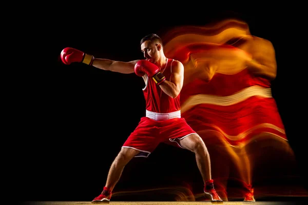 Retrato completo de um boxeador profissional em treinamento uniforme vermelho isolado sobre fundo preto. Um golpe certeiro. Luzes mistas — Fotografia de Stock
