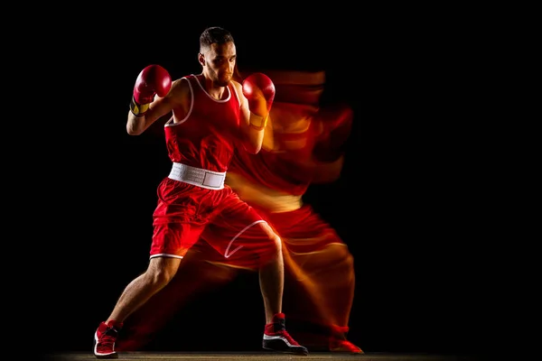 Boxeador profesional en entrenamiento uniforme rojo aislado sobre fondo negro. Efecto de luz mixta. Boxeador ambidextroso — Foto de Stock