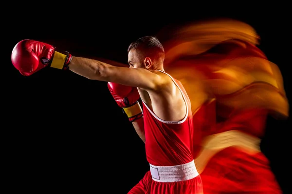 Gesneden portret van een professionele bokser in rood uniform training geïsoleerd over zwarte achtergrond. Rechtstreeks stoten. Gemengde lichten — Stockfoto