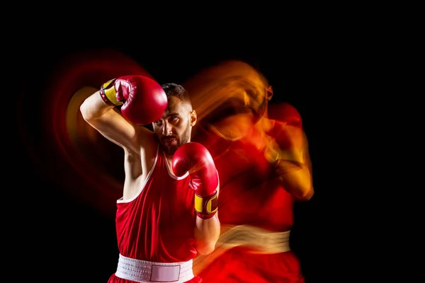 Jeden profesionální mužský boxerský trénink izolovaný nad černým backgrundem ve smíšeném světle. Klopýtá daleko od rány. Smíšený světelný efet — Stock fotografie