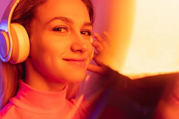 Detailní záběr mladé krásné dívky poslech hudby ve sluchátkách izolovaných přes gradient pozadí v neonových světel. Efekt Bokeh — Stock fotografie