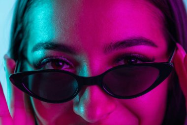 Modaya uygun güneş gözlüklü, mavi arka planda izole edilmiş güzel bir kız görüntüsü..