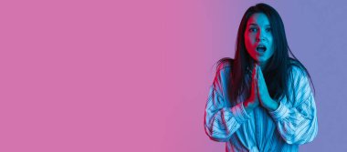 Güzel bir kızın portresi, neon ışıklarıyla izole edilmiş pembe bir arkaplanda. Şok olmuş yüz ifadesi. El ilanı