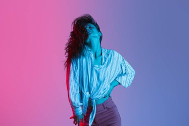 Güzel bir kızın hareketli portresi neon ışıklarıyla izole edilmiş pembe arka planda dans ediyor.