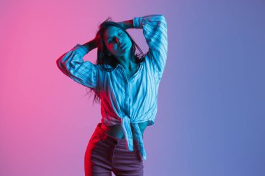 Güzel genç kız, neon ışıklarıyla izole pembe arka planda dans ediyor.