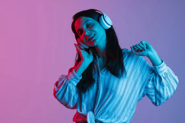 Портрет молодої красивої дівчини в навушниках ізольовані над градієнтним рожево-фіолетовим фоном в неонових вогнях — стокове фото