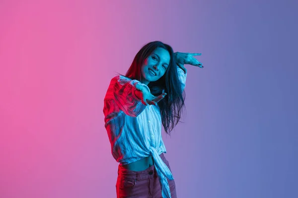Портрет у русі молодої красивої дівчини, що танцює ізольовано над градієнтним рожево-фіолетовим тлом у неонових вогнях — стокове фото