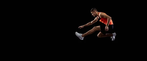 Jovem, atleta masculino em movimento isolado sobre fundo de estúdio preto. Vista lateral — Fotografia de Stock