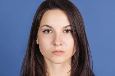 Mavi stüdyo arka planında izole edilmiş kameraya ciddi ciddi bakan güzel bir kadının yakın plan portresi.