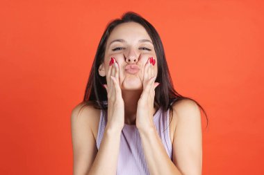 Kırmızı stüdyo arka planında yüzler çizen güzel genç bir kadının kırpılmış portresi.