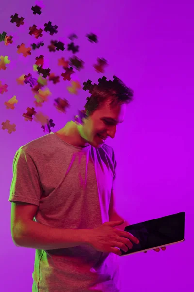 Современный коллаж кавказского мальчика с планшетом изолирован на фиолетовом фоне. Мужская голова состоит из кусочков головоломки. — стоковое фото