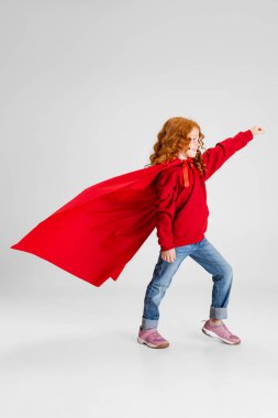 Kıvırcık kız portresi. Kırmızı mantolu çocuk. Gri arka planda ıssız bir yeri işaret ediyor..