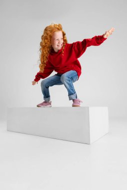 Küçük bir kızın portresi, gri stüdyo arka planında izole edilmiş sörfçü pozu veren çocuk..