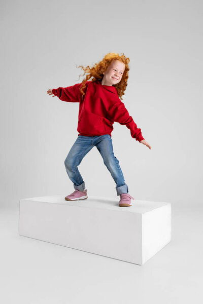 Portrait of little girl, child standing in pose of surfer isolated over gray studio background.