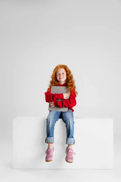 Full längd porträtt av lilla lockigt leende flicka, barn sitter med tablett isolerad över grå studio bakgrund. — Stockfoto