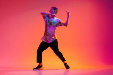 Yakışıklı sporcu çocuk neon ışıklı arka planda şık kıyafetler içinde hip-hop yapıyor..