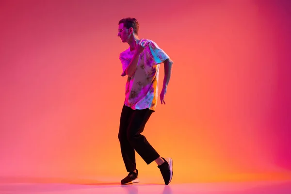 Full-length studio shot młodych kaukaski tancerz szkolenia hip-hop izolowane nad kolorowym tle gradientu w świetle neonu. — Zdjęcie stockowe