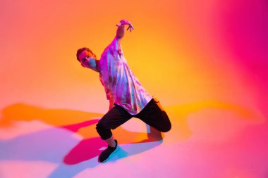Hip-hop dansı yapan genç sporcunun en iyi görüntüsü. Gradyan sarı stüdyo arkaplanındaki neon ışıklarıyla izole edilmiş.