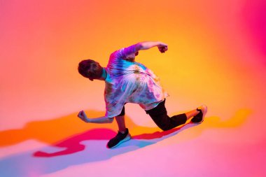 Hip-hop dansı yapan genç adamın en iyi görüntüsü. Gradyan sarı pembe stüdyo arka planında, neon ışıkta izole edilmiş.