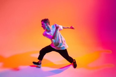 Sokak dansçısı. Hip-hop dansı yapan genç çocuk, neon ışıklı arka planda, gradyan sarı pembe stüdyo üzerinde izole edilmiş.