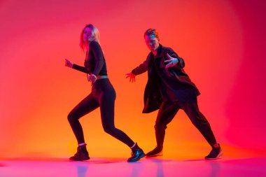 Oğlan ve kız neon ışıklı arka planda renkli siyah giysiler içinde hip-hop dansı yapıyorlar.
