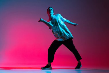 Genç hip-hop dansçısının tam boy yatay portresi. Neon ışıklarıyla izole edilmiş pembe arka plan üzerinde çalışıyor.