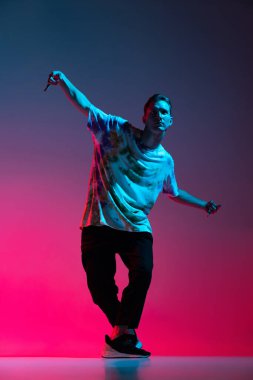 Hip-hop dansı yapan genç adamın dikey portresi neon ışıklarıyla izole edilmiş pembe arkaplanda izole edilmiş.